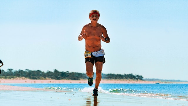 Starší muž v šortkách beží po pláži.jpg